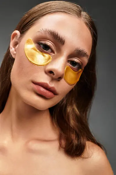 A young woman relaxes, applying gold under eye masks for a rejuvenating treat. — Stock Photo
