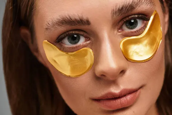 A young woman relaxes with golden eye patches, radiating confidence during her skincare routine. — Stock Photo