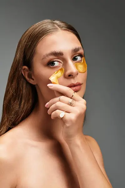 Young beautiful woman gently applying skincare patches in a minimalist studio setting. — Stock Photo