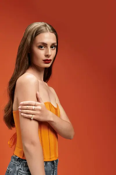 A young woman exudes charm and style in a vibrant orange setting. — Stock Photo