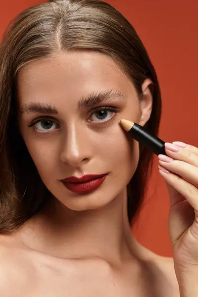 Young woman with sleek hair applies makeup in a vibrant studio filled with warm colors. — Stock Photo