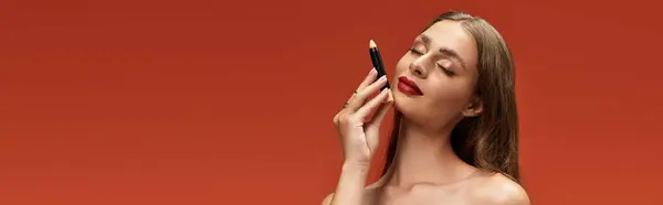 Woman showcases her beauty while applying makeup against a striking orange background. — Stock Photo