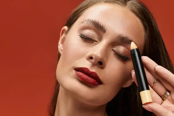 Young woman applies makeup with focus and elegance against a striking background color. — Stock Photo