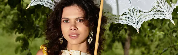 Молода жінка тримає парасольку в оточенні яскравої зелені, банер — стокове фото