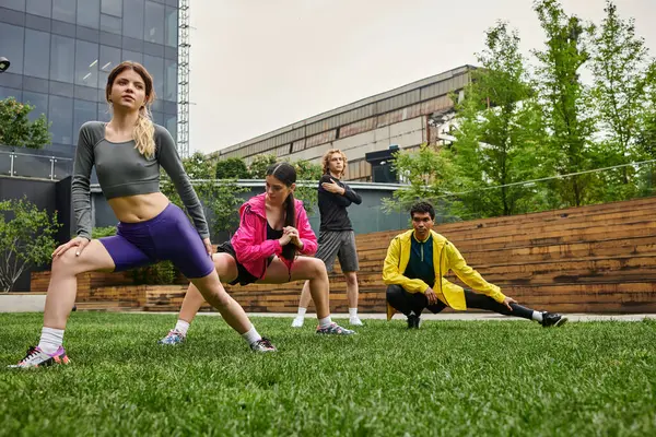 Группа молодых спортсменов делает динамичные растяжки в ярком городском парке. — стоковое фото