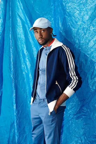 A stylish young man in athletic wear exudes confidence against a bright blue backdrop. — Stock Photo