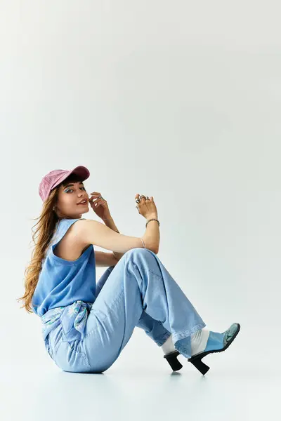 Молода жінка в модному вбранні сидить витончено в стильній позі, виключаючи впевненість і чарівність. — стокове фото