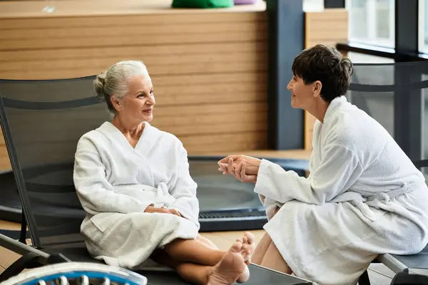 Dos hermosas mujeres maduras comparten un momento de alegría mientras se relajan en un centro de bienestar sereno. - foto de stock