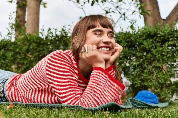 Молодая женщина улыбается на зеленом одеяле в солнечном саду. — стоковое фото
