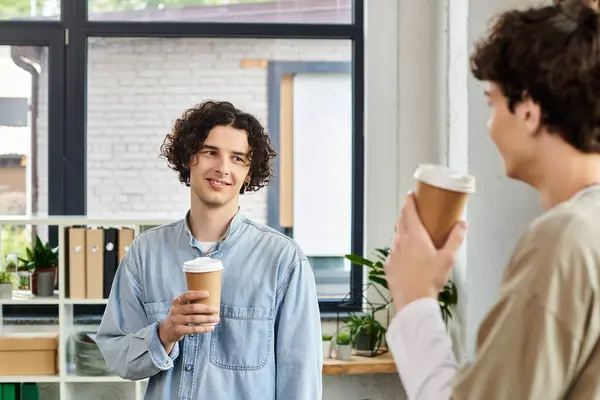 Due giovani colleghi godono di una conversazione amichevole mentre tengono tazze di caffè nel loro spazio di lavoro. — Foto stock