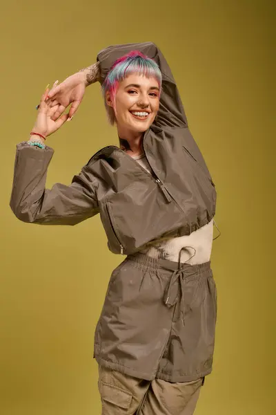 Una joven con el pelo corto colorido posa alegremente en un estudio moderno lleno de luz. - foto de stock