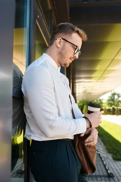 Молодой учитель-мужчина стоит на улице в кампусе, держа чашку кофе и теряясь в мыслях. — стоковое фото