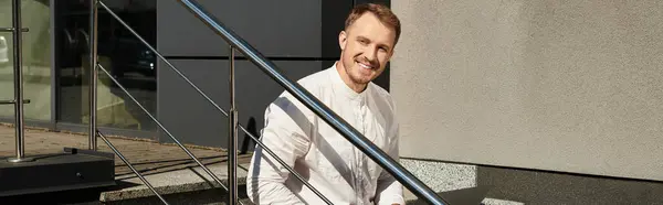 A young man dressed smartly sits on steps, smiling and radiating enthusiasm for teaching. — Stock Photo
