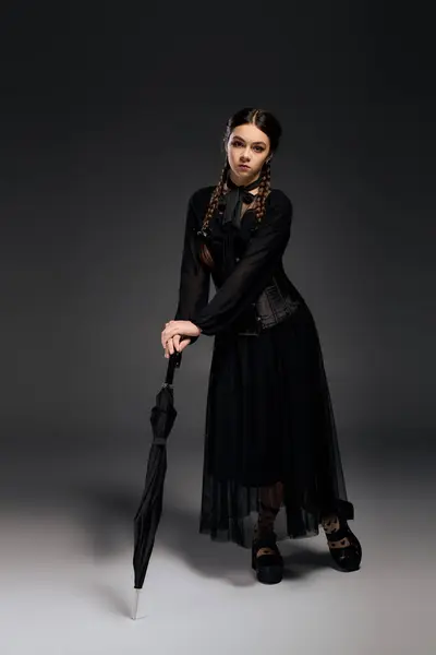 Uma menina em um vestido preto quarta-feira com tranças posa com um guarda-chuva, celebrando o Halloween — Fotografia de Stock