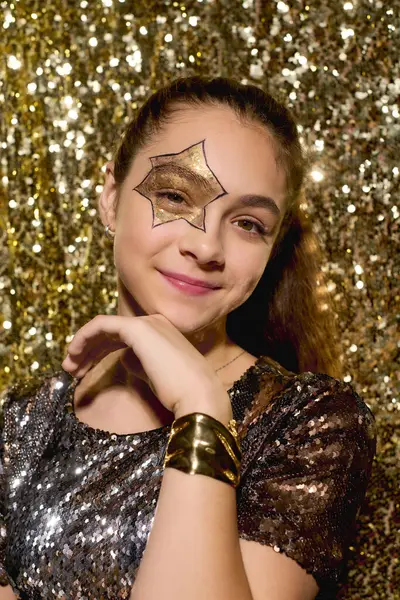 Una ragazza con una stella disegnata sulla guancia posa allegramente tra lucide paillettes d'oro durante Halloween. — Stock Photo