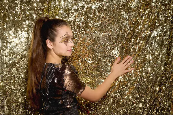 Una ragazza affascinante con una stella sulla guancia gioca con lucenti paillettes d'oro ad Halloween. — Stock Photo
