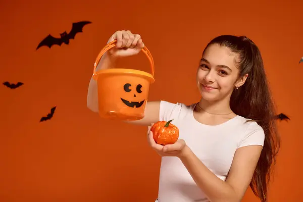 Menina expressa alegria para o Halloween, segurando uma abóbora e balde em uma configuração festiva. — Fotografia de Stock