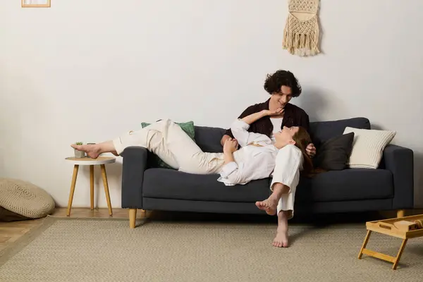 A curly-haired man and a beautiful woman share a joyful moment on their couch in a modern apartment. — Stockfoto