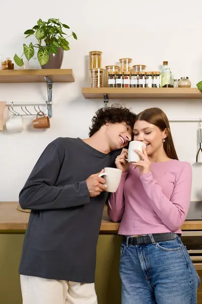 A young couple shares a joyful moment, sipping coffee and smiling in their modern kitchen. — Stockfoto