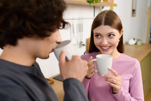 A joyful young couple shares a moment over coffee in their modern apartment, smiling at each other. — Stockfoto