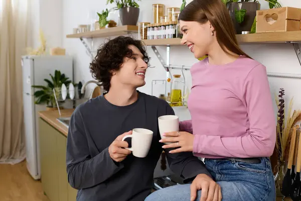 A curly-haired man and a woman share a happy moment with mugs in their stylish home. — стоковое фото