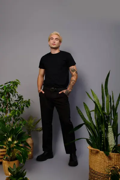A young handsome man stands proudly among indoor plants, showcasing youth culture and style. — Stock Photo