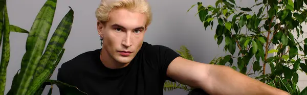 Молодой красивый мужчина демонстрирует молодежную культуру в яркой зеленой обстановке с растениями. — стоковое фото