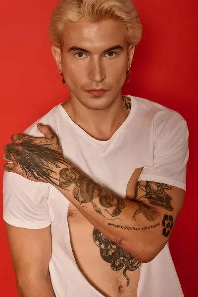 Adolescente guapo posa con confianza, destacando tatuajes impresionantes contra un telón de fondo llamativo. - foto de stock