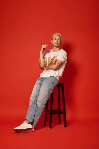 Стильный подросток задумчиво позирует на стуле, демонстрируя молодежную культуру и модные тенденции. — стоковое фото