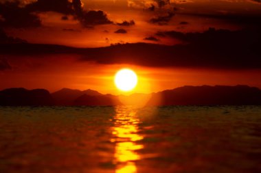 Güneş ve parıltı gün batımında gökyüzünde kara bulut ve siluet dağlarıyla altın çağda gölde.