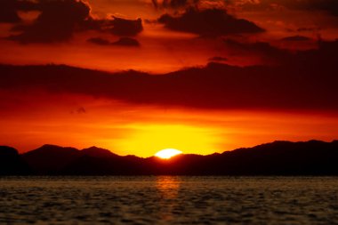 Gölde altın çağda, kara bulut ve siluet dağlarıyla gün batımı.