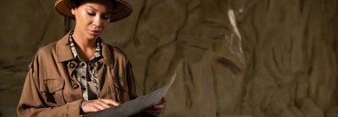 Bej ceketli genç arkeolog çöldeki antik haritayı işaret ediyor.