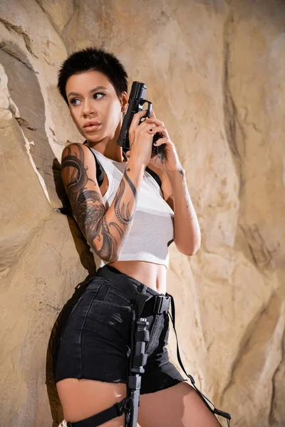 Morena Arqueólogo Tatuado Sosteniendo Pistola Mientras Esconde Detrás Roca Cueva — Foto de Stock