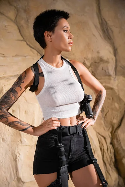 Seksi kıyafetli silahlı arkeolog elleri kayaların yanında duruyor. 