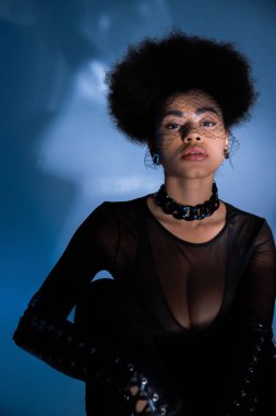 Siyah peçeli şık Afro-Amerikan kadın mavi poz verirken kameraya bakıyor. 