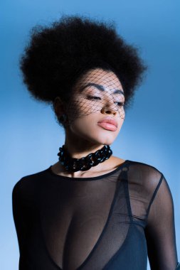 Siyah peçeli ve seksi giyinmiş Afro-Amerikalı genç bir kadının portresi mavide poz verirken gözlerini kaçırıyor. 
