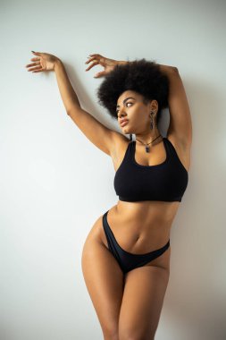 Ekin bluzlu ve iç çamaşırlı seksi Afro-Amerikalı kadın duvarın yanında poz veriyor. 