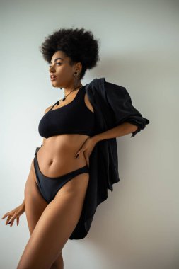 Beyaz duvarın yanında iç çamaşırlı, Afro-Amerikan bir kadın poz veriyor. 