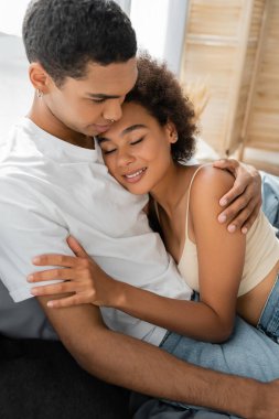 Güzel ve kıvırcık gözlü bir kadın. Yatak odasında Afrikalı Amerikalı erkek arkadaşına sarılıyor.
