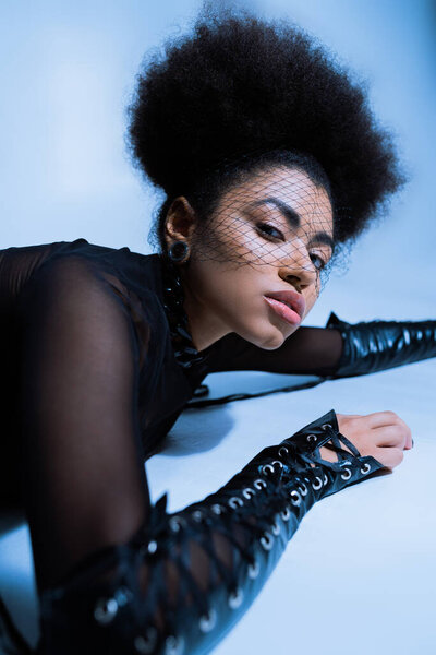 молодая африканская американка в черной вуали смотрит в камеру, лежа на синем 