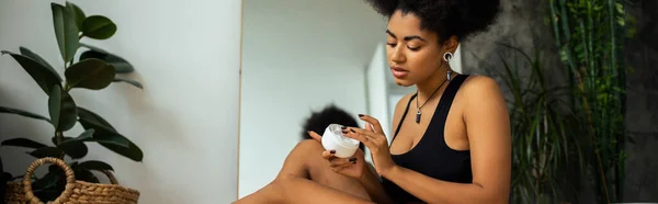 Femme Afro Américaine Bouclée Tenant Crème Cosmétique Près Miroir Plante — Photo