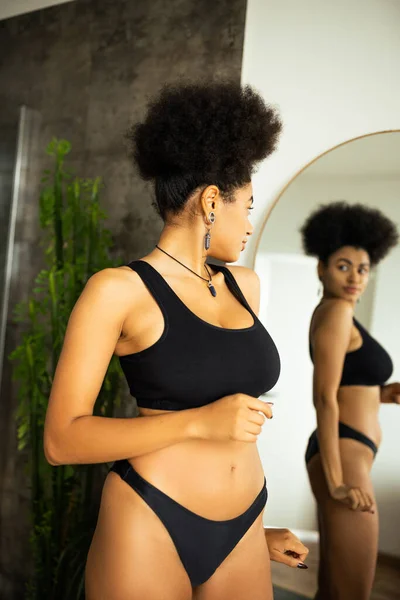 穿着内衣裤的卷曲的非洲裔美国女人在家里看着模糊的镜子的侧视图 — 图库照片
