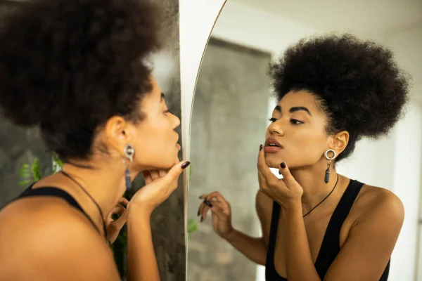 バスルームで鏡を見ながら顔に触れるアフリカ系アメリカ人女性のぼやけた側面図 — ストック写真