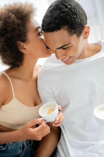 年轻的非洲裔美国女人 拿着咖啡杯对着家里微笑的男朋友说秘密 — 图库照片