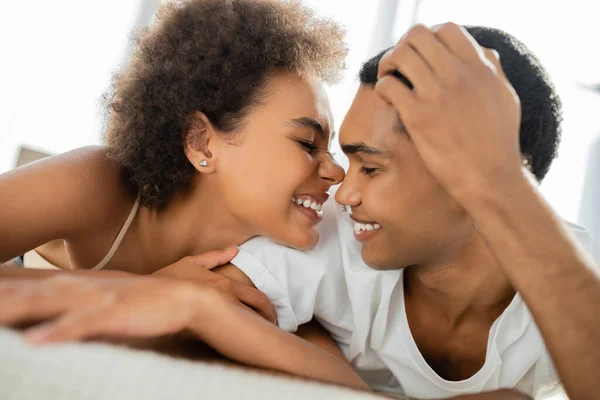 明るいアフリカ系アメリカ人の女性がベッドの上で笑顔のボーイフレンドの近くで — ストック写真