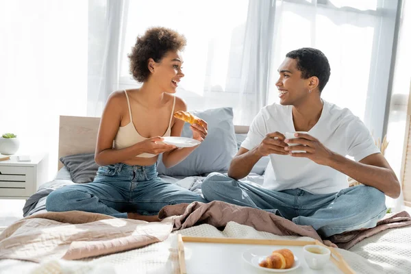 快乐的非洲裔美国夫妇在床上吃早餐时互相望着对方 — 图库照片