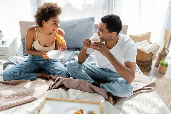 快乐的非洲裔美国夫妇在卧室吃早餐时用羊角面包喝咖啡 — 图库照片