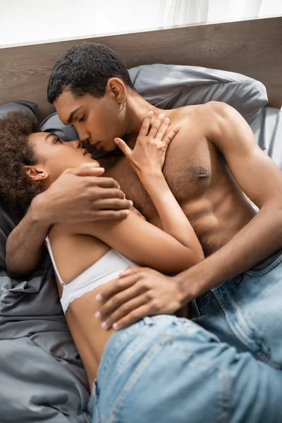 top view of muscular african american man hugging and kissing seductive girlfriend on bed