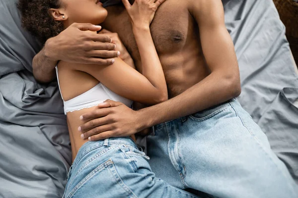 对穿着牛仔裤躺在床上抱着床的年轻夫妇和充满热情的非洲裔美国人的偏见 — 图库照片