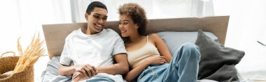 Neşeli Afro-Amerikalı kadın evde yatakta yatıyor ve genç erkek arkadaşına gülümsüyor.